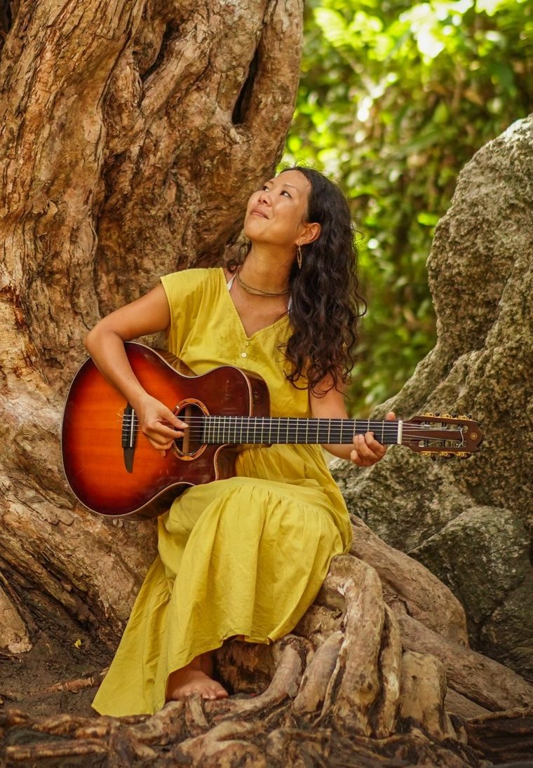 Akari Tamura playing guitar under a tree
