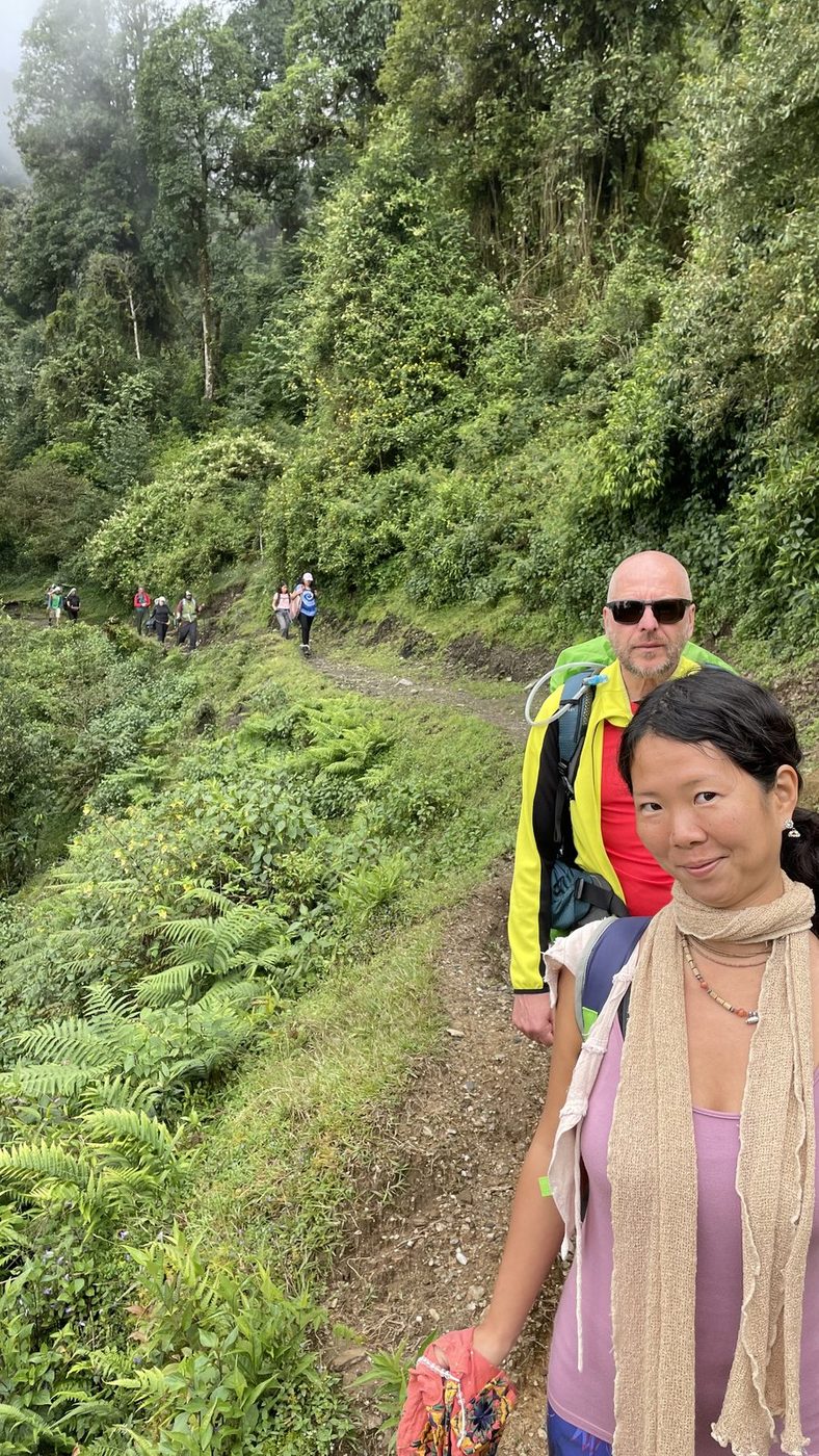 Two trekkers smiling on a narrow path through green forest