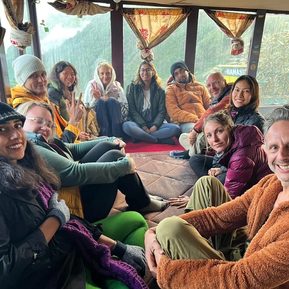 A group of trekkers sitting in a circle on cushions inside a lodge, smiling at the camera