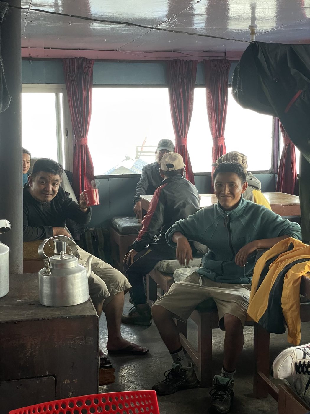 Guides and trekkers sitting around a table with a kettle inside a mountain lodge