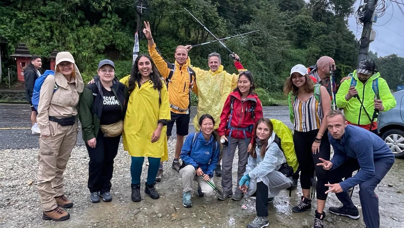 A group of trekkers in rain jackets and ponchos posing together on a wet road at the start of the trail