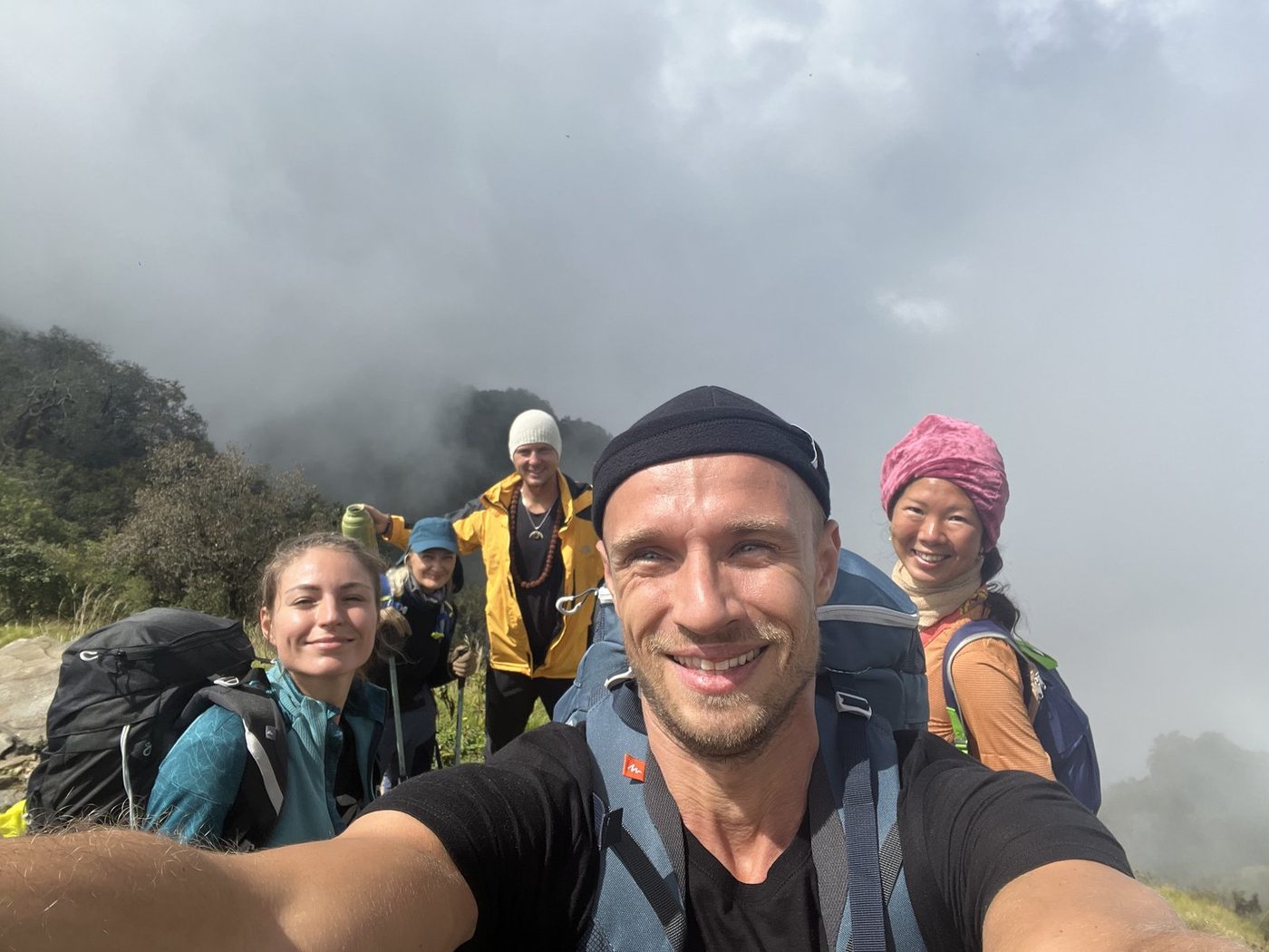 Five smiling trekkers in a selfie with low cloud behind them