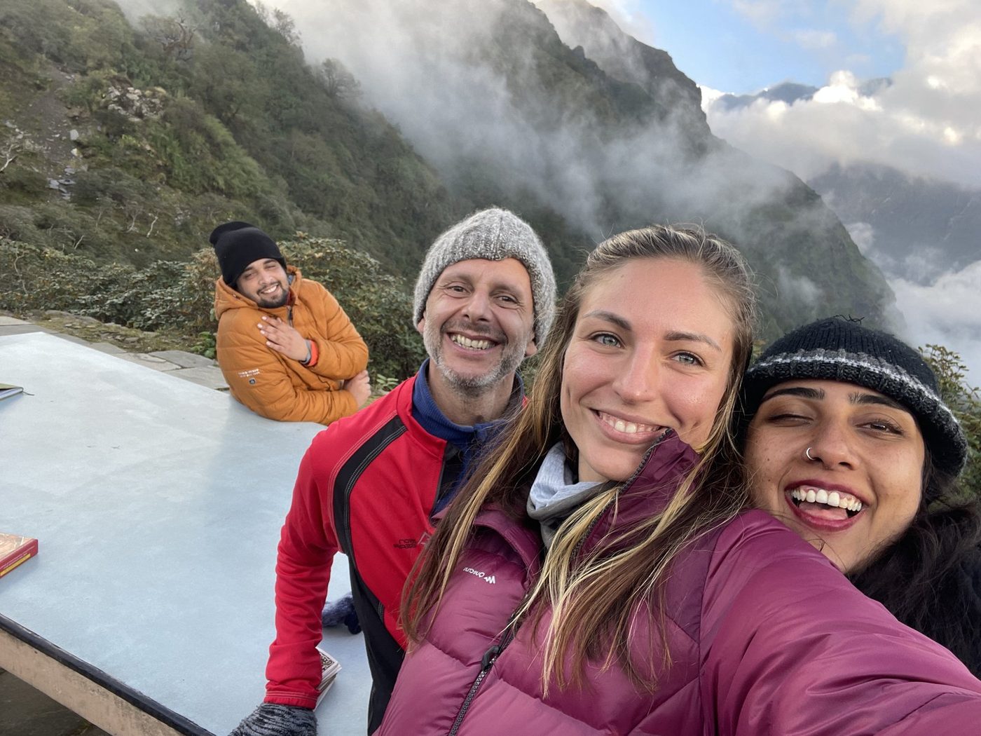 Four friends smiling in a selfie on a rooftop above a misty mountain valley