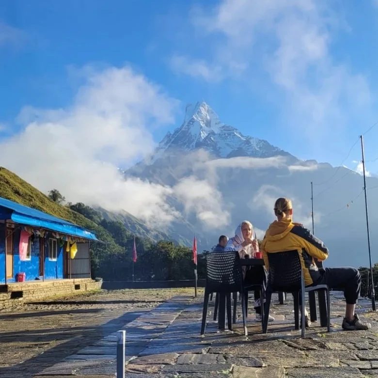 Two people having tea at a table on a stone terrace, with a pointed snow peak behind them