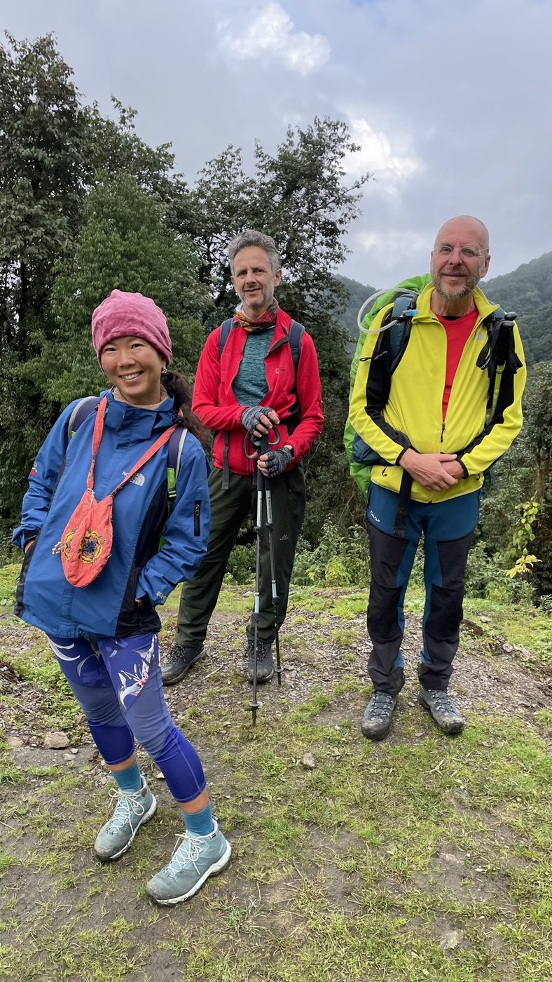 Three trekkers in bright jackets standing together on a green hillside