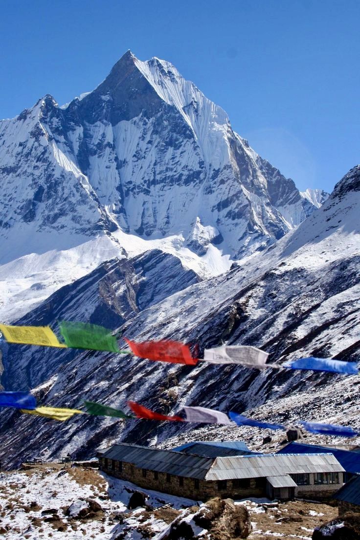 Colorful prayer flags below a sharp white peak, with a lodge in the snow