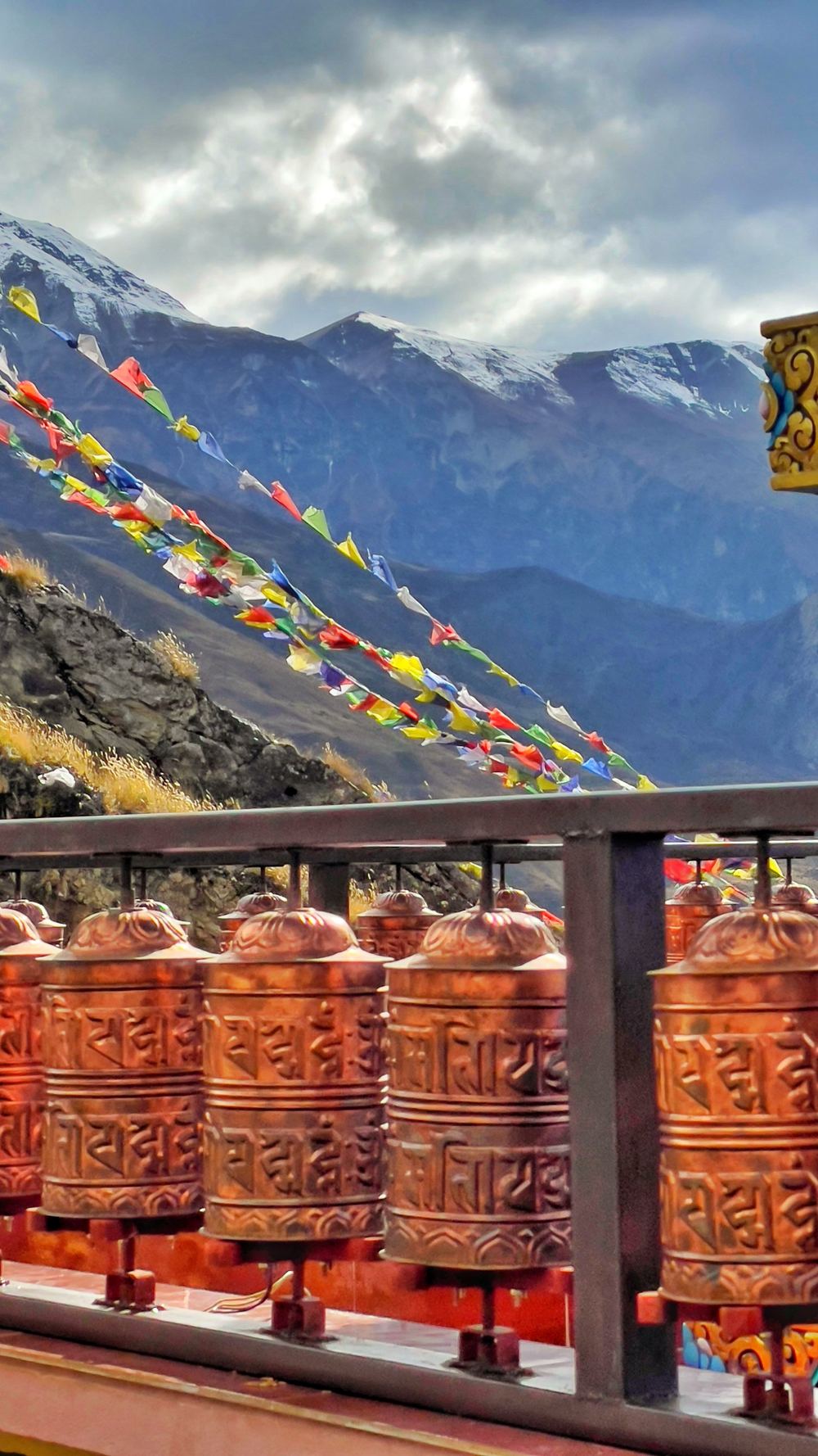 Copper prayer wheels with prayer flags and snow mountains behind