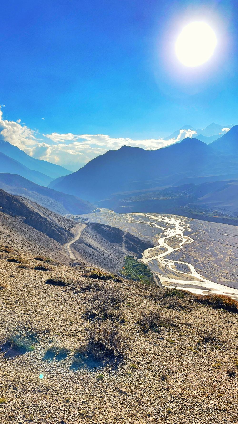 A river braiding through a wide valley with the sun above the ridge